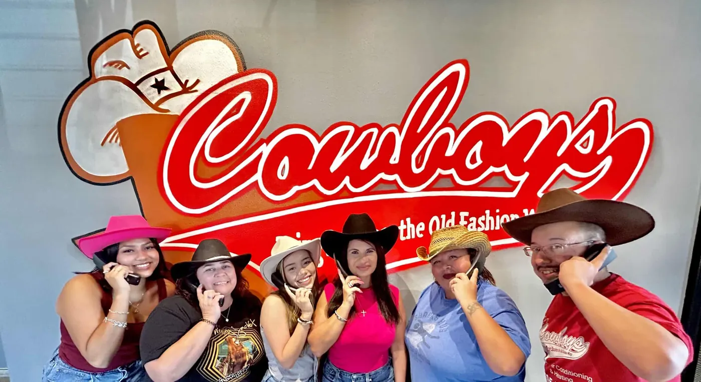 The Cowboy's office team in cowboy hats in front of the Cowboys sign